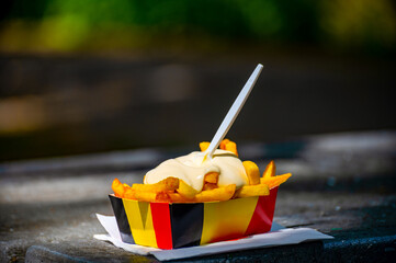 Paper box in colors of Belgian flag with fried potato frit chips and mayonnaise sauсe.