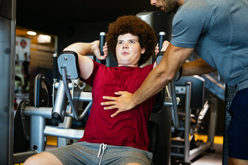 Fat young men with trainer exercising at fitness gym.