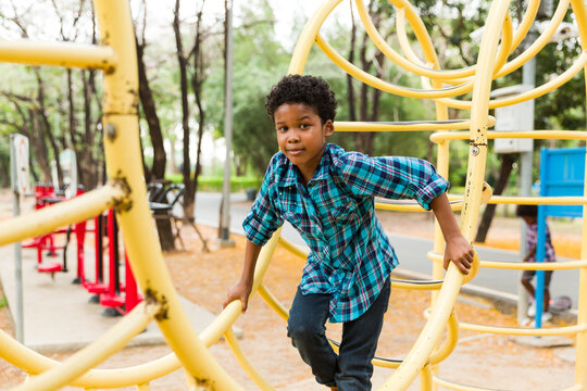 African American young boy smiling and playing at the playground in the city park, looking at camera.