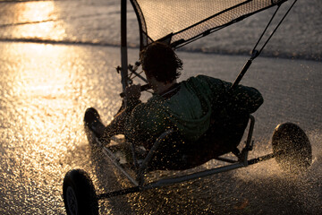 Rear view of person riding a sand yacht along a sandy beach at sunset.