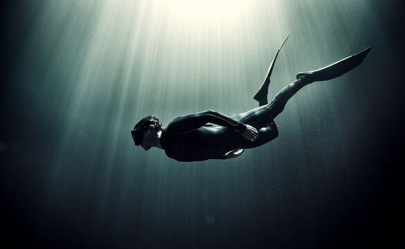 Underwater view of diver wearing wet suit and flippers, sunlight filtering through from above.