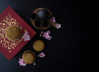 Mooncake flatlay on wooden table. Traditional Baked Mooncake on Dark Background. Mooncakes with Sakura Flowers. 