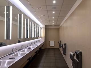 Wash-basins and hand dryers in a modern restroom with large mirrors
