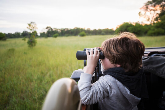 Fototapeta A six year old boy using binoculars seated in a safari jeep.