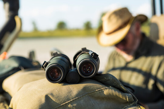 Binoculars on the dash of a safari jeep, a safari guide in the background.