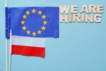 Search for employees, recruitment after crisis and coronavirus. we are hiring-wooden letters on blue background. flatly with copy space. new hiring positions. EU and Polish flags,work abroad