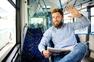a young passenger in a bus sits reading a newspaper and waving to a passerby