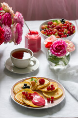 Curd pancakes with berry curd served with tea on a table decorated with bouquets of roses.