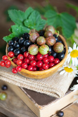 Red and black currant, gooseberry in ceramic bowl on a wooden background