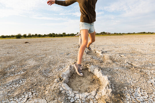 Thirteen year old girl leaping into elephant footprints, Nxai Pan, Botswana