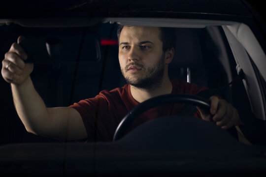 A handsome bearded man adjusts the rear view mirror before starting to move. Responsible driver, safe driving. Preparing the car for the trip.