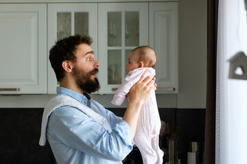 Modern father in his arms holds his little child while standing in the kitchen