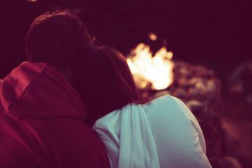 Portrait of a loving married couple sitting by the fire in nature. A man hugs a woman, view from...