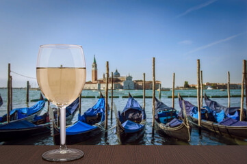 Glass of white wine with view of gondolas pier row anchored on Canal Grande with San Giorgio Maggiore church in the background, Venice, Italy