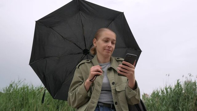 Woman with parasol sitting alone on a rainy day with a smartphone in hand