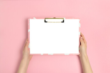 Female hands hold clipboard. Blank mockup on a pink pastel background.