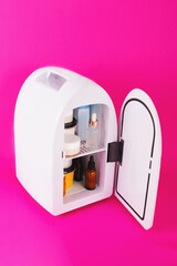 Mini fridge for keeping skincare, makeup and beauty product cool and fresh. Extend shelf live of creams, serums. Keep your beauty products organized and cool. Vivid magenta background.