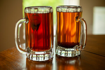 Close up image of two large glass beer mugs filled with fresh black tea. Mugs are sitting on an open window sill with trees in the background.