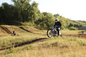Fototapeta na wymiar Man in white helmet riding motorbike on rough terrain while moving down hill on track