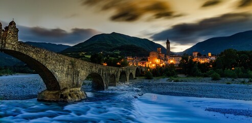 Bobbio, Piacenza/Italy - Jun 7th 2020: sunset view of Bobbio village and its Old Bridge (Devil Bridge), Emilia Romagna region - obrazy, fototapety, plakaty