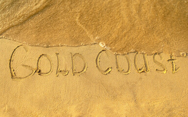 Gold Coast words written on beach sand with water wave. Gold Coast inscription is written on a sand. One of the most famous tourist destination in Australia. 