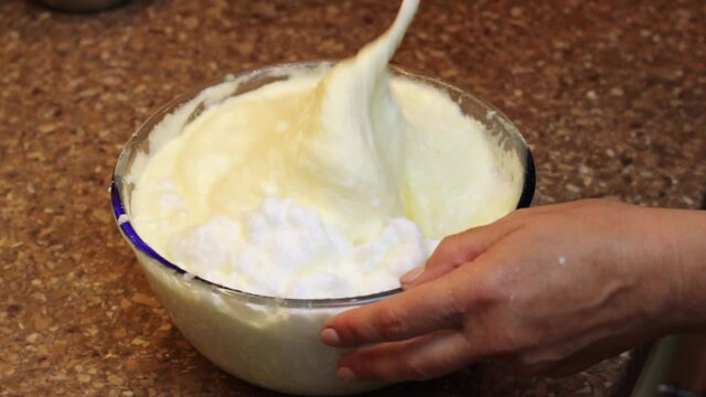 Slowly mixing whipped egg yolk and white for baking a sponge cake in a glass bowl