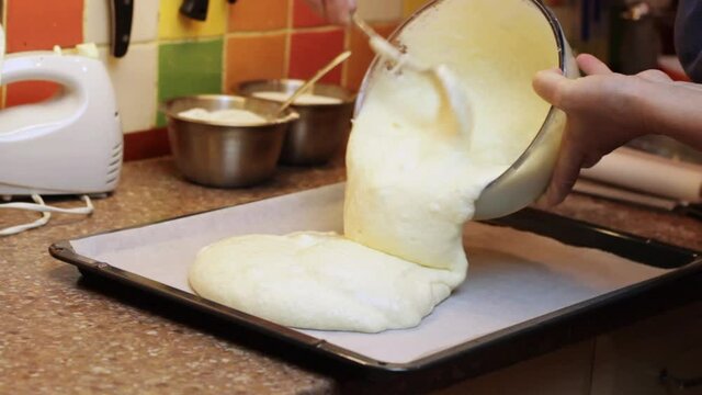 Spooning batter for baking a sponge cake onto a baking tray with greasing paper