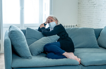 Depressed senior widow woman with protective mask alone at home feeling sad and missing family