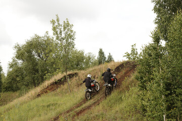 Rear view of extreme motorcyclists in helmets reaching speed while climbing hill on rough road
