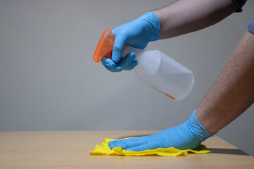 Hand with a sprinkler and the other hand with a glove cleaning a table with a cloth. Furniture...