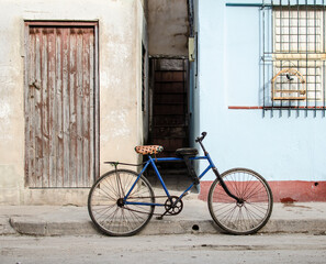 Fototapeta na wymiar Blue bike bicycle in front of Cuban house with singing bird in cage, red and light blue facade, wooden door and window