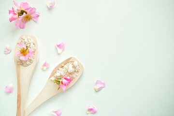 Bath salt in wooden spoons with flowers and rose petals, on a white background. The view from the top.