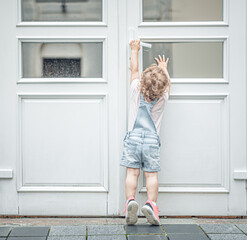 The child tries to open the door. The child reaches for the doorknob on the street. - obrazy, fototapety, plakaty