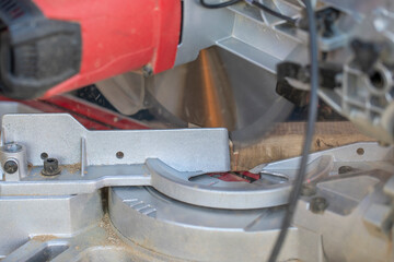 A sharp rotating circular saw blade cuts the oak beam into pieces. Wood processing with professional tools. Shavings and sawdust fly during the cut. Home workshop concept.