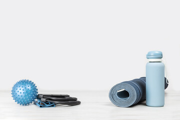 Rolled blue yoga mat and exercise resistance band water bottle on grey wooden surface. Gender neutral fitness and exercise concept with copy space. Active lifestyle and sport. Workout at home or gym
