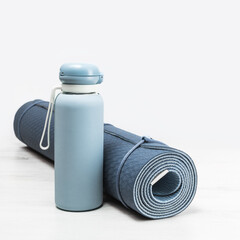 Rolled blue yoga mat and blue water bottle on grey wooden surface. Gender neutral fitness yoga and exercise concept with copy space. Active lifestyle. Workout at home or gym
