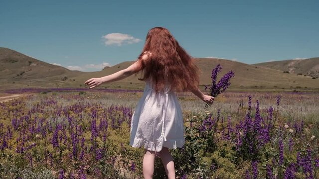 A caucasian beautiful wonan dancing on the beautiful field during summer day. The woman wears beautiful dress. The woman is smiling. SLOW MOTION