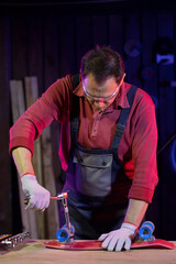 middle-aged brunette man in jumpsuit fixing red plastic kids skateboard in home workshop with socket wrench. jack of all trades concept