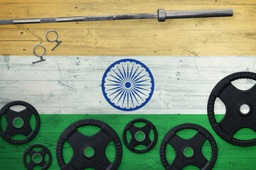 India gym concept. Top view of heavy weight plates with iron bar on national background.