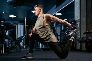 Fototapeta na wymiar Bodybuilder stretching on floor in gym.