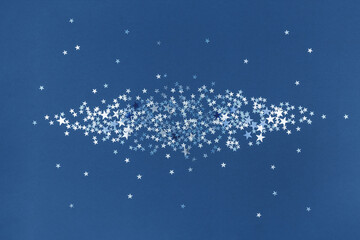 Blue scattered silver holographic glitter confetti star shaped on blue background. Flat lay top...