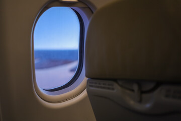 Fototapeta premium Close up of oval airplane window and back of economy seat with blue sky. transportation and Travel Concept.