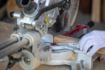 Fototapeta premium A carpenter cuts a timber beam with a circular saw. A closeup of hands in gloves. A sharp rotating disc that cuts through wood. Shavings and sawdust fly.