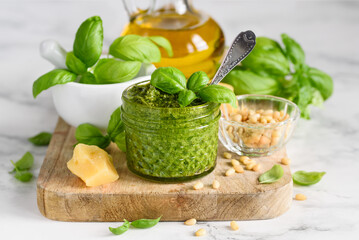 Homemade basil pesto sauce in a glass jar on a wooden board. Ingredients.  Vegetarian food. Selective focus - obrazy, fototapety, plakaty