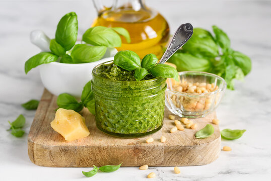 Homemade basil pesto sauce in a glass jar on a wooden board. Ingredients.  Vegetarian food. Selective focus