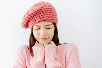 Portrait of young Asian woman in knitted sweater closes eyes and holding her hands underneath the chin isolated over white background. Woman's face closeup. Concept woman lifestyle and winter.