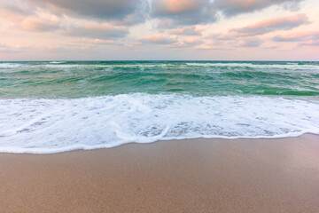cloudy sunset sea side. waves running the sandy beach. changing windy weather in evening light