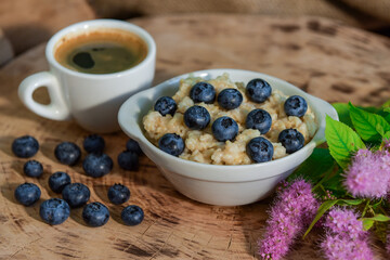 Oatmeal with blueberries for breakfast with coffee on a wooden table. Traditional healthy breakfast. Oatmeal and espresso. Close-up