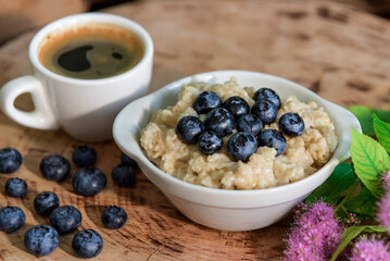 Oatmeal with blueberries for breakfast with coffee on a wooden table. Traditional healthy breakfast. Oatmeal and espresso. Close-up