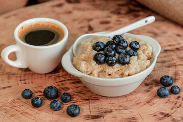 Oatmeal with blueberries for breakfast with coffee on a wooden table. Traditional healthy breakfast. Oatmeal and espresso. Close-up